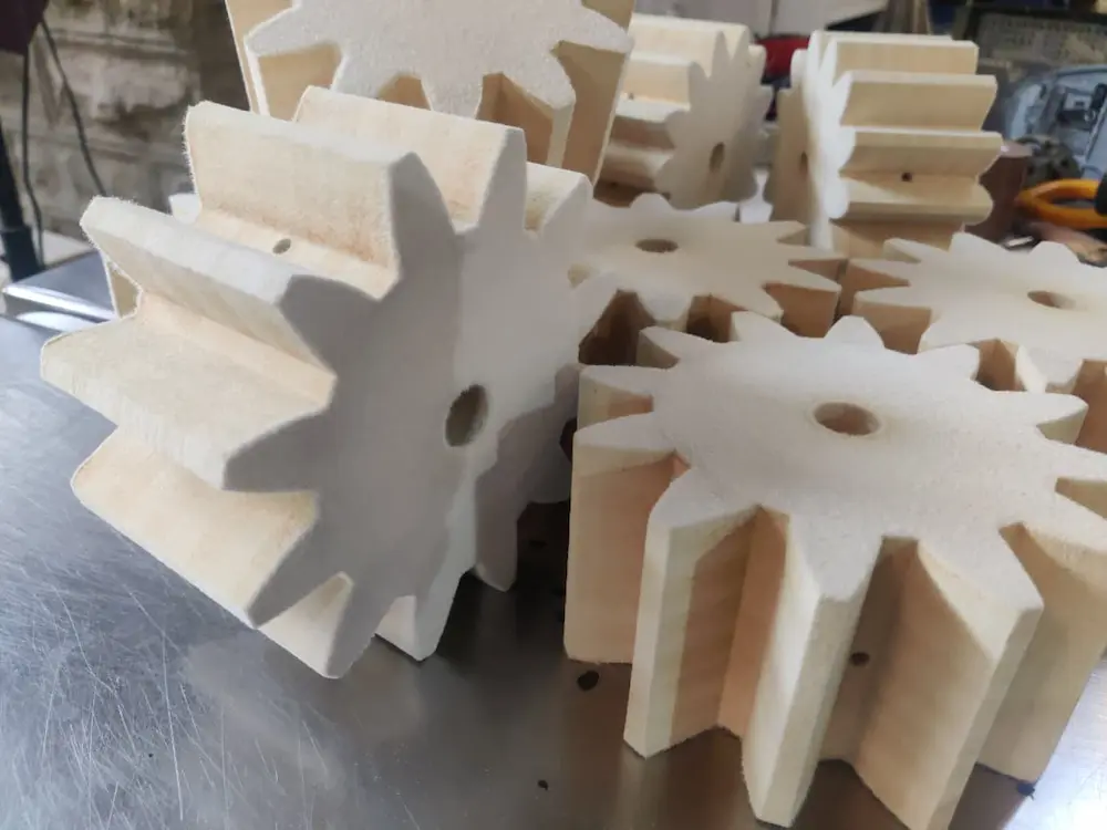 British Felt Wooden gears with thick teeth stacked together on a metal surface in a workshop.
